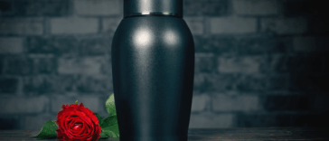 A black urn with a rose laying down next to it.