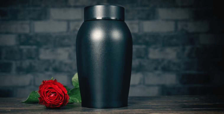 A black urn with a rose laying down next to it.