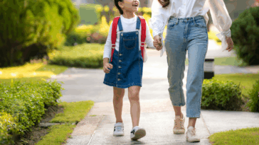 A woman holding a little girl's hand walking down the sidewalk.