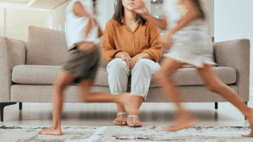 A woman sitting on the sofa with children running around her.
