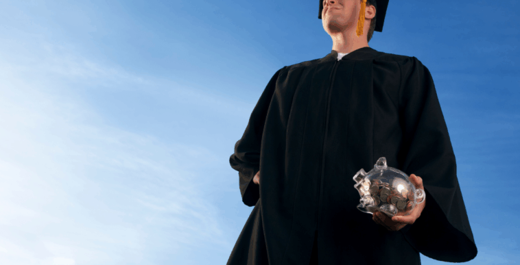 A graduate holding a piggy bank looking off into the sky.