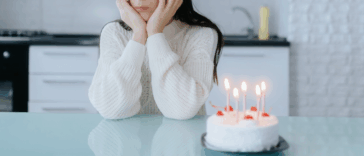 A woman sitting at a counter behind a birthday cake with candles in it.