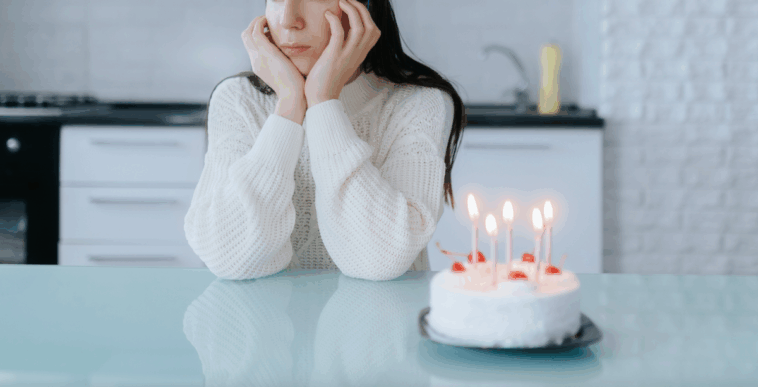 A woman sitting at a counter behind a birthday cake with candles in it.