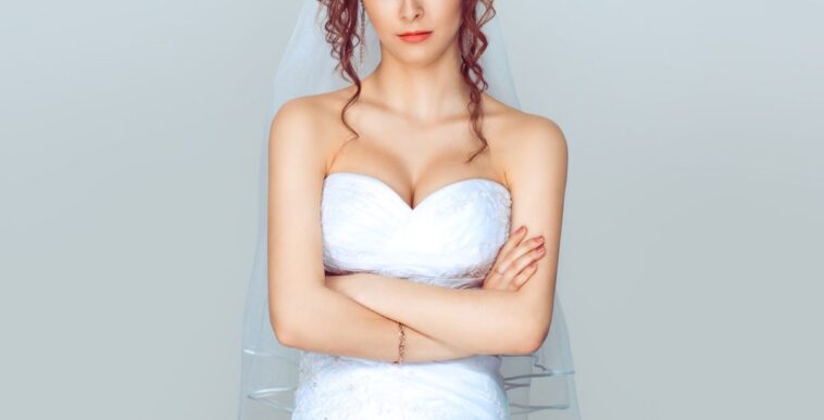 Grumpy bride. Sad and disappointed hesitating woman in wedding dress, arms folded, unhappy wife.