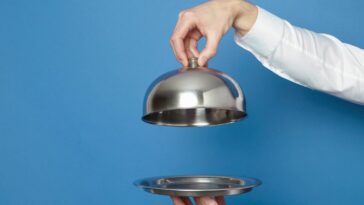 Man holding silver tray and lid against blue and green background.