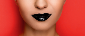 A woman with black lipstick in front of a red background.