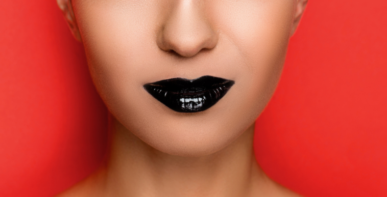 A woman with black lipstick in front of a red background.