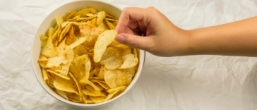 A child's hand taking a potato chip from a bowl.