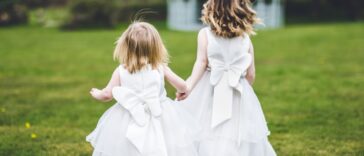 Back shot of flower girls holding hands and running in the grass.