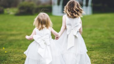 Back shot of flower girls holding hands and running in the grass.