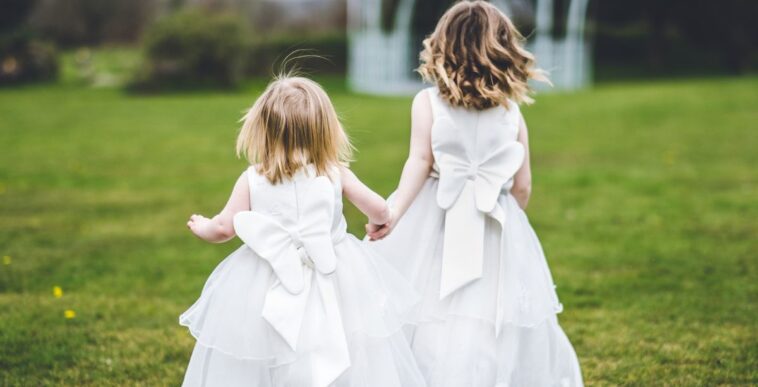 Back shot of flower girls holding hands and running in the grass.