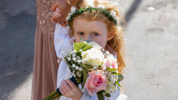 A little girl wearing a floral crown, and holding a bouquet in front of her face.
