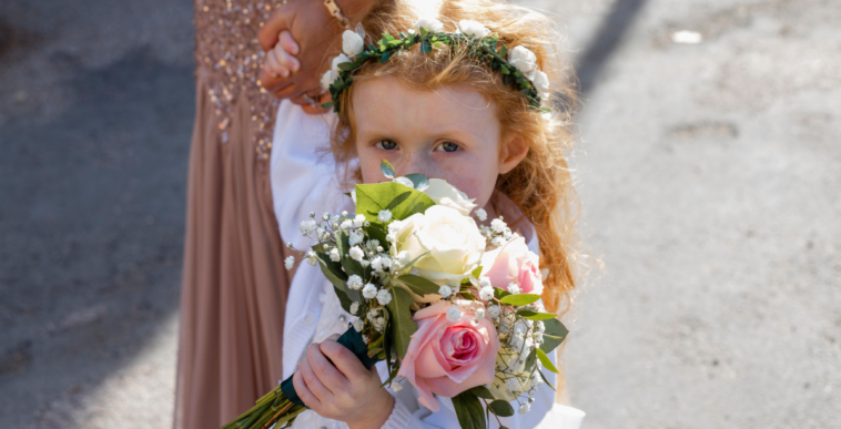 A little girl wearing a floral crown, and holding a bouquet in front of her face.
