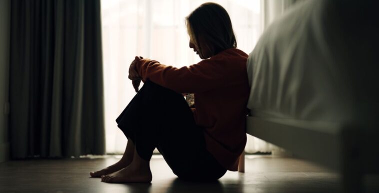 Silhouette of a woman, sad and depressed, sitting on the bedroom floor.