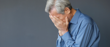 A man with gray hair holding his head in his hands.