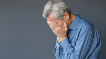 A man with gray hair holding his head in his hands.