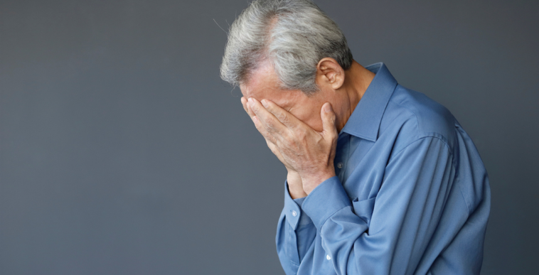 A man with gray hair holding his head in his hands.