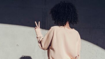Rear view of a young woman making a peace sign. On the wall you can see the shadow of the woman.
