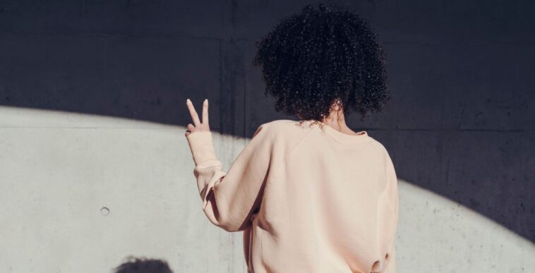 Rear view of a young woman making a peace sign. On the wall you can see the shadow of the woman.