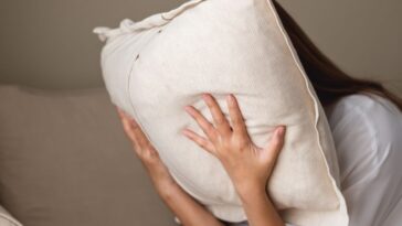 A depressed, stressed woman putting her face in a pillow.