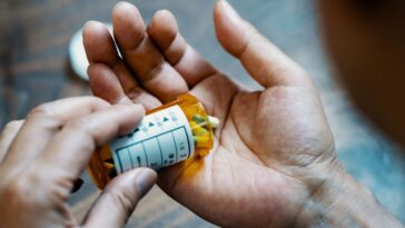 Close-up of a male hand holding, a pill bottle, pouring medication into his hand.