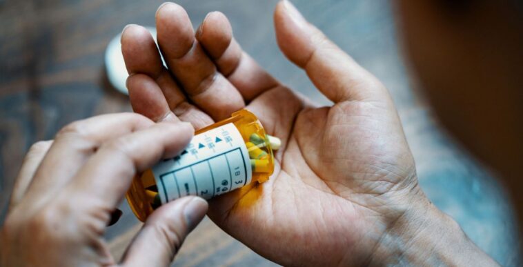 Close-up of a male hand holding, a pill bottle, pouring medication into his hand.