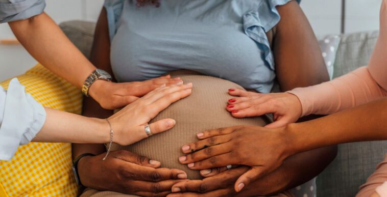 Group of female friends touching stomach of pregnant woman at baby shower. Close up.