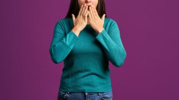 Front view of a shocked woman looking in the camera, against a purple background in a studio shot.
