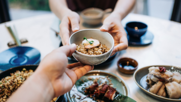 Two people sharing a number of small plates of food.