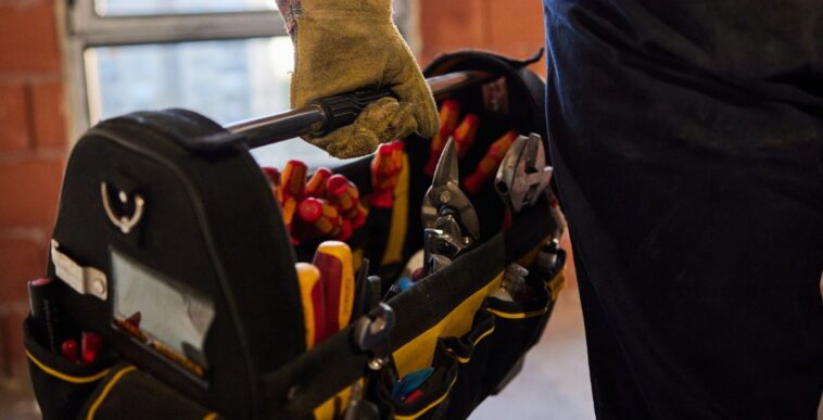 Close up of an unrecognizable electrician carrying toolbox at construction site.