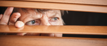 A woman peering through shades out a window.