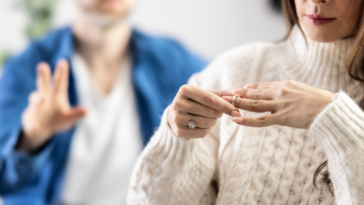 A woman taking off her ring with a man standing in the background.
