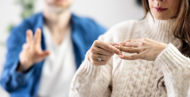 A woman taking off her ring with a man standing in the background.