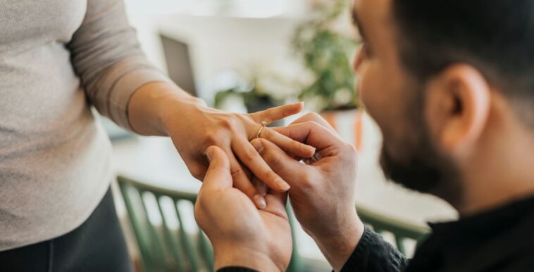 Romantic man puts an engagement ring on girlfriend's finger at home.