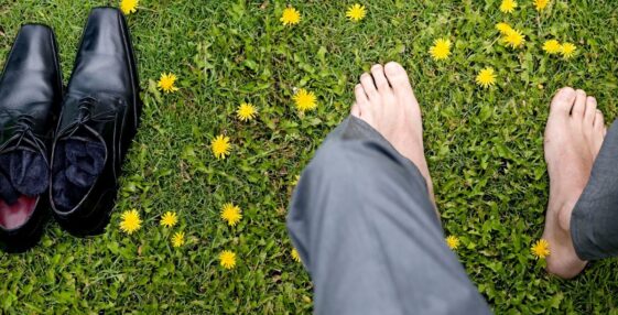 Shot of a man's feet in the grass. His black, dress shoes sit next to him.