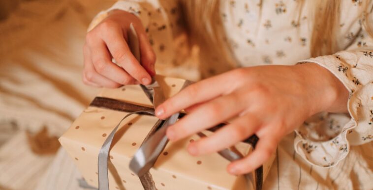 Hands untying a ribbon on a polka dot gift box.