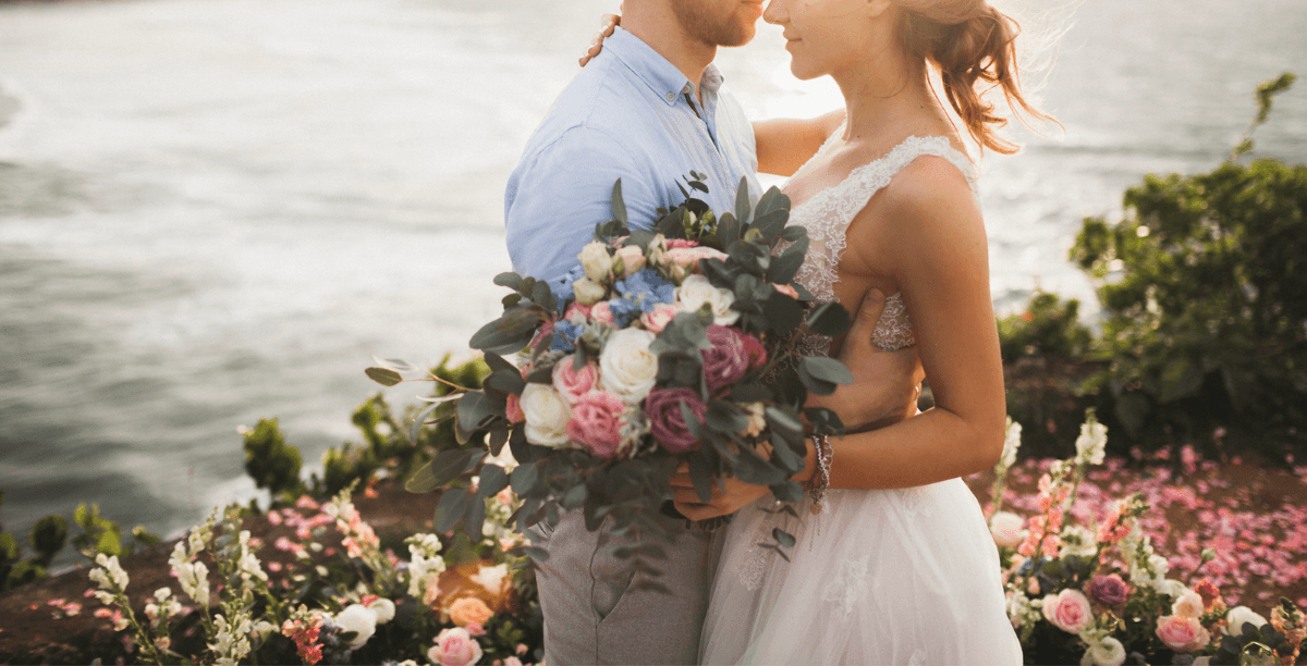 A bride and a groom embracing with the ocean in the background.