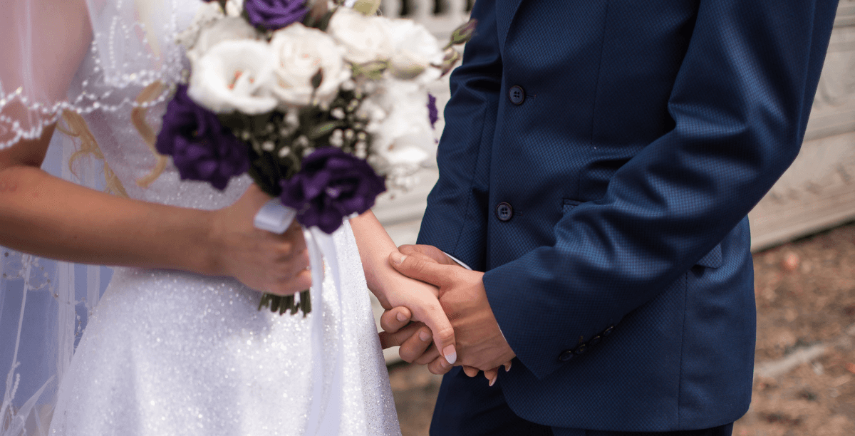 A woman in a wedding dress holding as bouquet holding a man's hand.