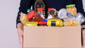 A man holding a cardboard box full of non-perishable food.