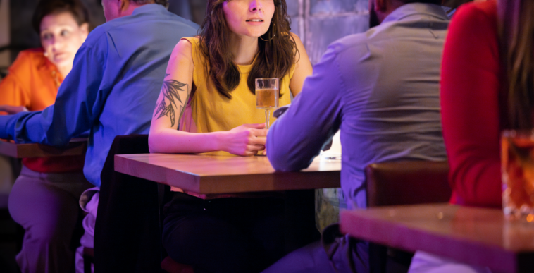 A woman in a yellow tank top with an arm tattoo sitting across a table form a man.