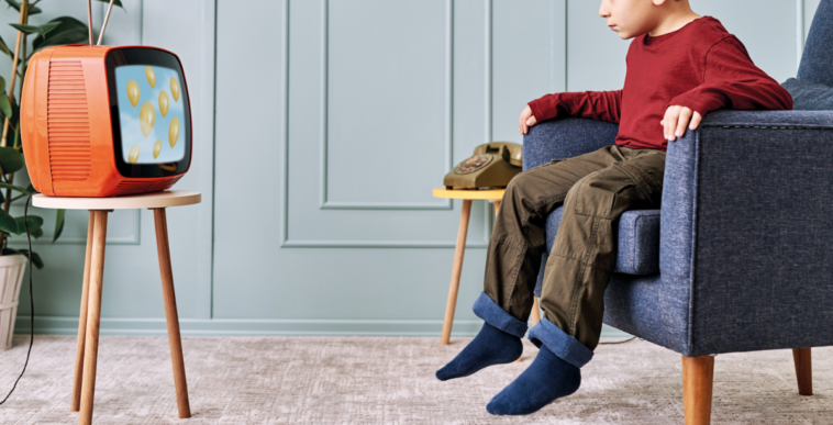 A little boy sitting in a chair and watching television.