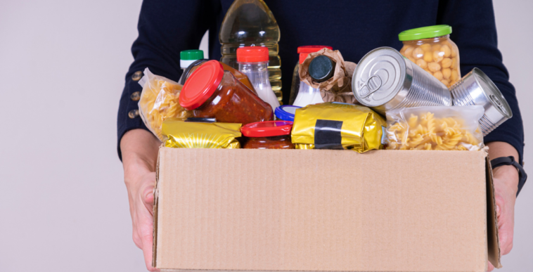 A man holding a cardboard box full of non-perishable food.