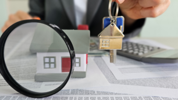 Aman holding a key above paperwork with a magnifying glass in front.