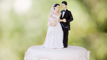 A wedding cake with a bride and groom cake topper on top.