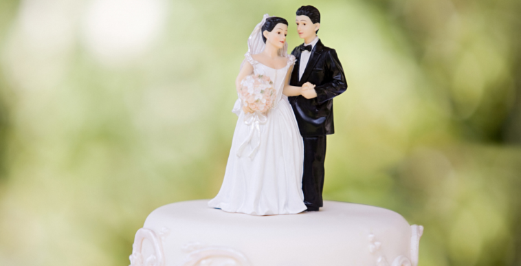 A wedding cake with a bride and groom cake topper on top.