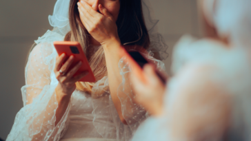 A bride looking at a smart phone and covering her mouth.