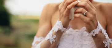 A woman in a wedding dress wiping tears from her eyes.