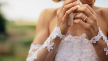 A woman in a wedding dress wiping tears from her eyes.
