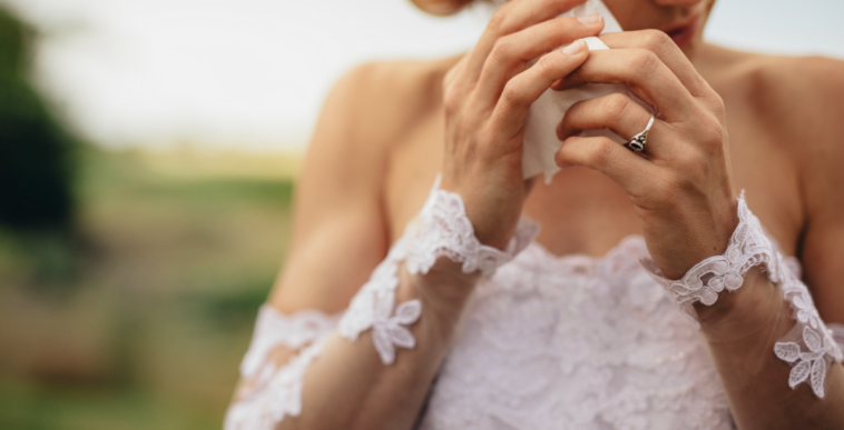 A woman in a wedding dress wiping tears from her eyes.