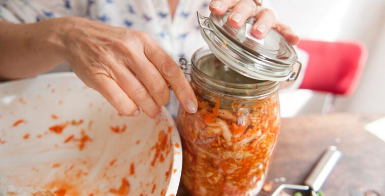 Woman closing the swivel top mason jar with all the mixed ingredients (and a weight) for a healthy fermented, originally Korean, side dish: kimchi.